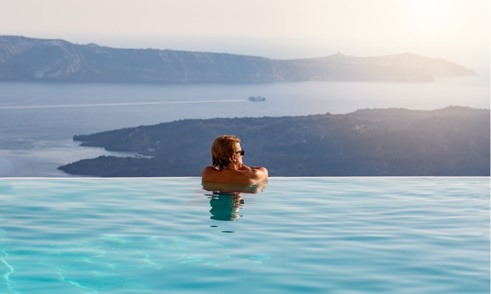 man relaxing in infinity swimming pool looking at the sea view picture id903400912